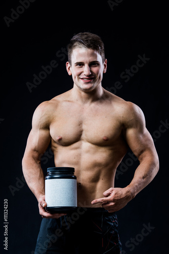 Fotografia Bodybuilder holding a black plastic jar blank white label whey protein and point