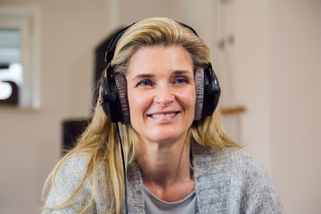 people, technology and leisure concept - happy middle-aged woman sitting on sofa with smartphone and headphones listening to music at home