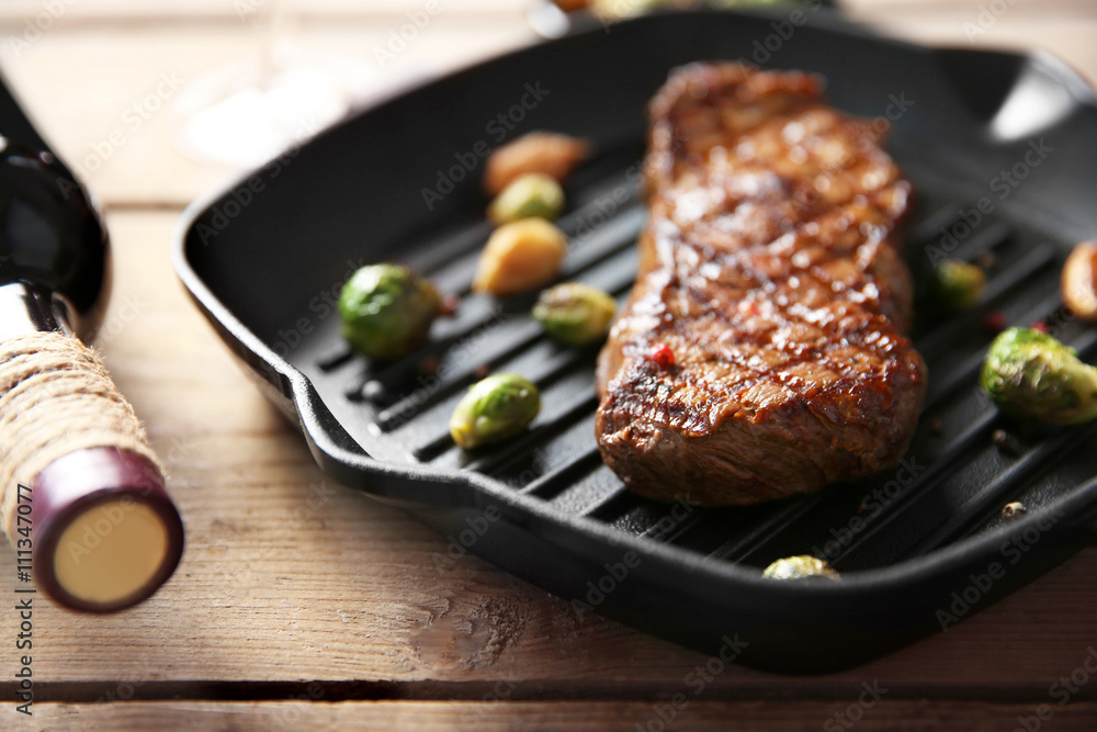Grilled steak on grill pan with wine on wooden table