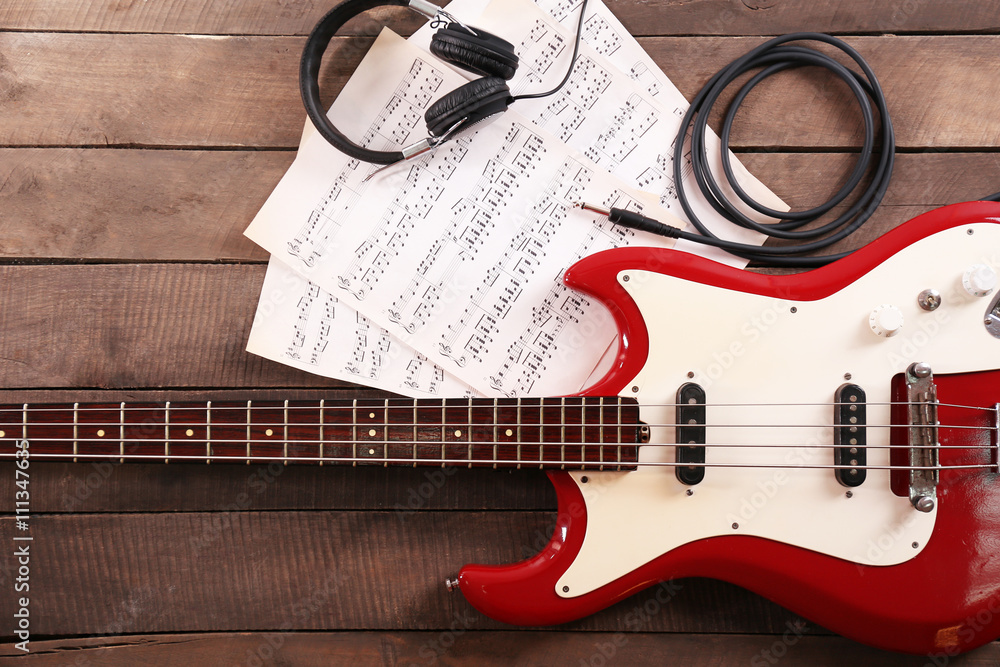 Electric guitar with notes and headphones on wooden background