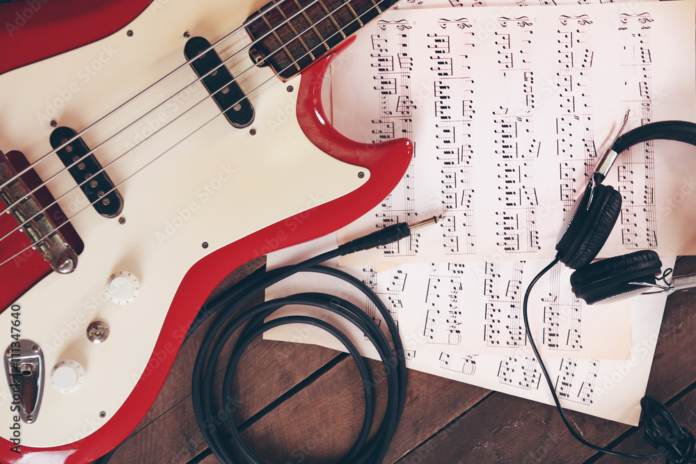 Electric guitar with notes and headphones on wooden background