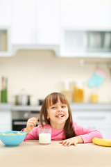 Poster - Beautiful little girl having breakfast with cereal, milk and banana in kitchen