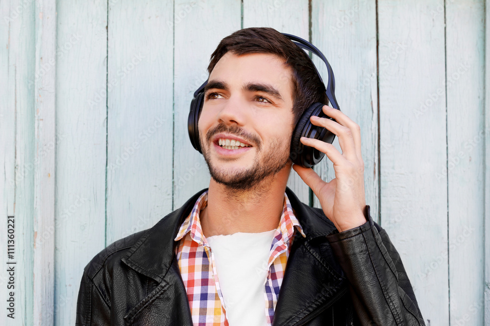 Young man listening to music on a house wall background