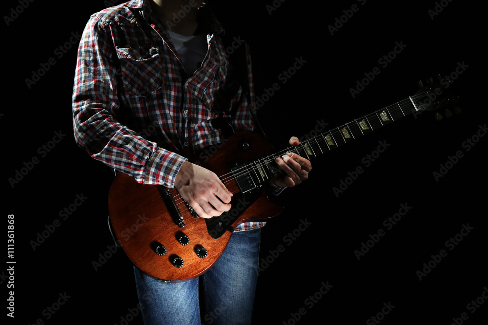 Young man playing electric guitar on lighted dark background