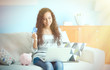 © Africa Studio - Beautiful young girl with credit card, piggy bank and laptop on couch