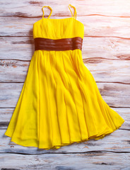 Wall Mural - Yellow summer dress. Yellow dress on wooden background. Woman's garment for warm season. Stylish piece of clothing.