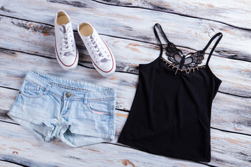 Wall Mural - Denim shorts with dark top. Black top and canvas shoes. Light denim shorts on table. Female clothing from catalog.