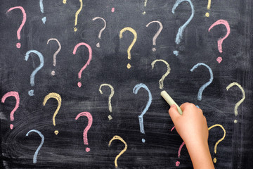 Child drawing colorful question marks on blackboard