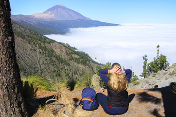 Young  girl with his backpack siting on the rock and contemplating the landscape of volcano Teide on Tenerife. Concept for travel o tourism