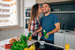 Young couple preparing salad in the kitchen. Woman is kissing ma