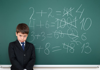 school boy decides examples math wrong on chalkboard background, education concept
