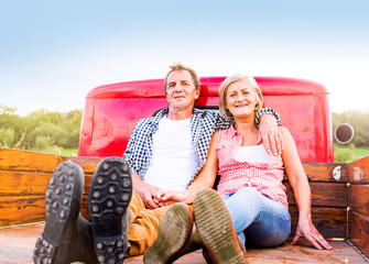 Senior couple sitting in back of red pickup truck