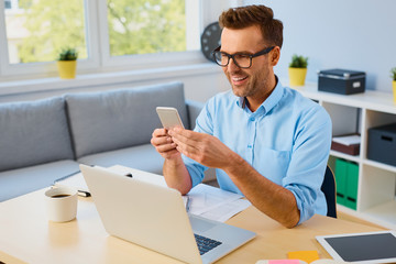 Wall Mural - Happy man paying bills with his phone at home