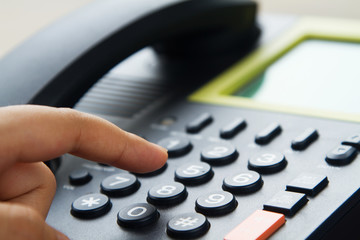 Close up hand dialing telephone, office of call center service for customer concept.