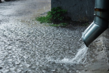 Rain Water Flowing From A Metal Downspout During A Heavy Rain. Concept Of Protection Against Heavy Rains