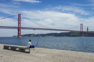 Fisherman on embankment of Tejo river with The 25 de Abril Bridge on background. Lisbon, Portugal