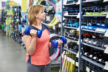 Woman Chooses Dumbbells For Fitness In Sports Shop