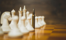 Closeup Photo Of Bullet In Row Of White Chess Pieces On Wooden B