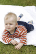Adorable funny laughing baby boy relaxing on a white blanket in a green summer garden 