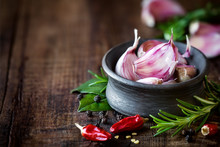 Cloves Of Purple Garlic In A Black Bowl With Rosemary, Bay Leaf, Black Pepper And Chili Pepper On Dark Rustic Wooden Background. With Plenty Of Copy Space For Your Text
