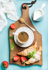 Wall Mural - Breakfast or dessert set. Freshly baked croissants with strawberries, cup of coffee and milk in creamer on brown wooden board