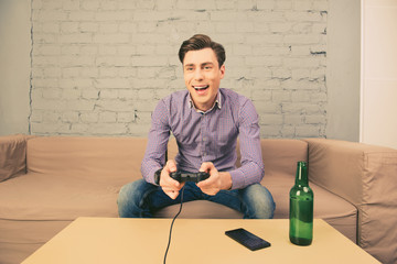 Excited  man sitting on sofa with bottle of beer and playing vid