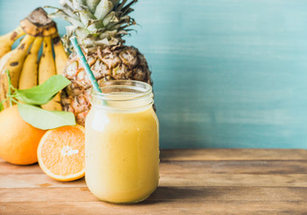 Freshly blended yellow and orange fruit smoothie in glass jar with straw