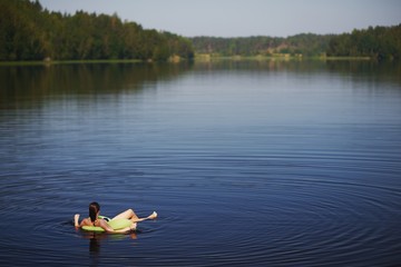 relaxed young woman lying on inflatable ring in lake and admiring the stunning views. Away on a blurred background forest and sky. Top view .