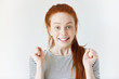 Close up isolated portrait of cheerful young redhead woman looking and gesturing at the camera with happy and winning expression, achieving life goals. Beautiful freckled teenage girl with no makeup