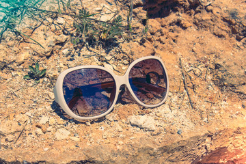 White retro sunglasses with dark glasses on the rock mountain and rocky coast background on a sunny day.