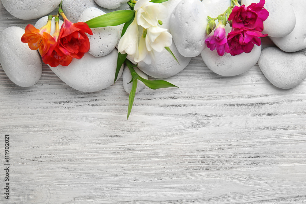 Spa stones for therapy with flowers on white wooden background