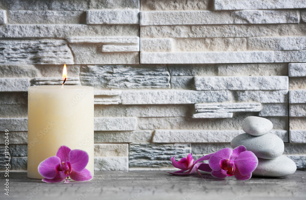 Composition of spa pebbles, flowers and candle on grey brick wall background