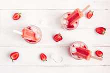 strawberry popsicle, sliced strawberries and ice on a white wooden background, flat lay, top view