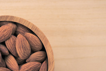 Almonds in brown bowl on wooden background