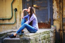 Brunette Girl Sitting In A Blue Shirt With Stripes And Jeans In The City