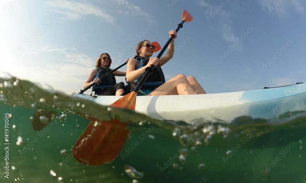Two young women paddling blue kayak - obrazy, fototapety, plakaty 