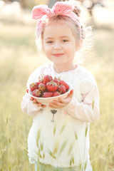 Poster - Smiling child girl 4-5 year old eating strawberry outdoors. Looking at camera. Summer season.