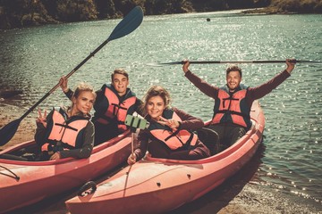 Cheerful friends taking selfie in kayaks on a beach.