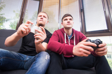 Friends and video games. Two handsome young men playing video games while sitting on sofa