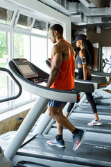 Black african american athletic couple running on treadmills in gym