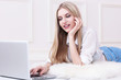 © MaxFrost - Happy young woman lying on the floor at home and using laptop