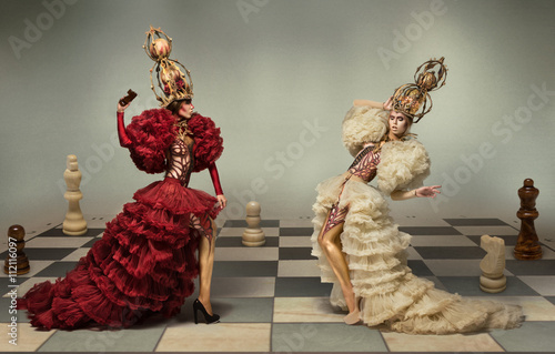 Fotografering Battle of chess queens on chess board with chess figures on background