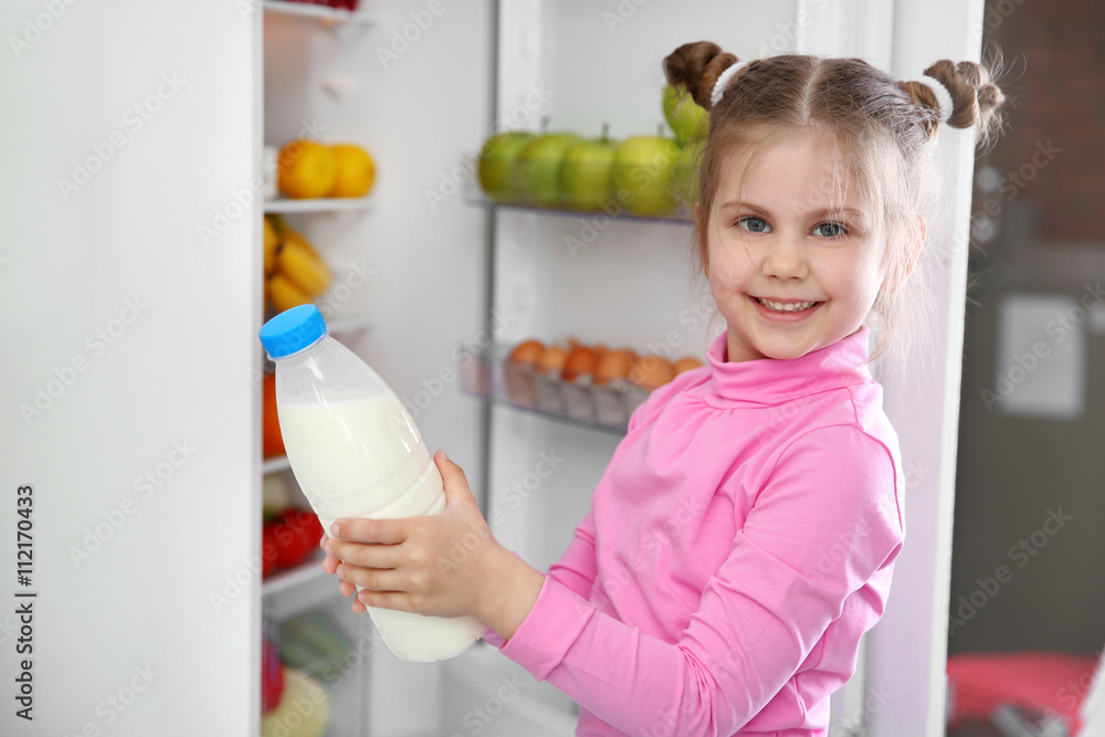 Little girl taking bottle milk from the fridge