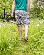 © koldunova - Man goes according forest trail and carries in her hand scooter, on the background green of grass and trees spring day