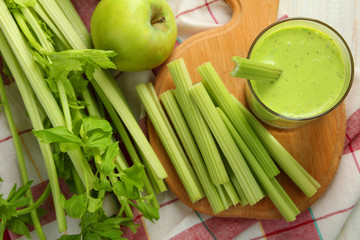 Wall Mural - Fresh green celery juice in glass on wooden cutting Board near green Apple on the brown wooden background