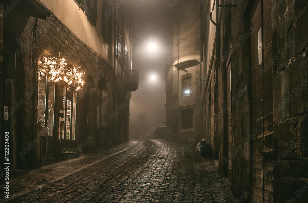 Old European narrow empty street of medieval town on a foggy evening. Taken in Bergamo, Citta Alta, Lombardia - obrazy, fototapety, plakaty 