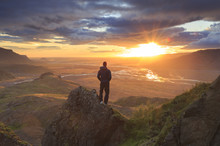 Man Standing On A Ledge Of A Mountain, Enjoying The Beautiful Sunset Over A Wide River Valley In Thorsmork, Iceland.