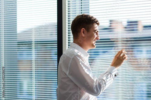 Business Man In A Suit With Cufflinks Looking Out Of Window Through The Blinds Waiting Concept Near Big Office Window Background With Copy Space For Your Text Message Or Promotional Content