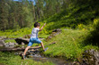 Little boy jumps over a stream in a forest