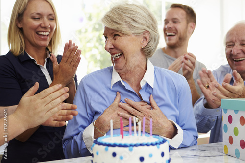 Plakat Senior Woman Blows Out Birthday Cake Candles At Family Party